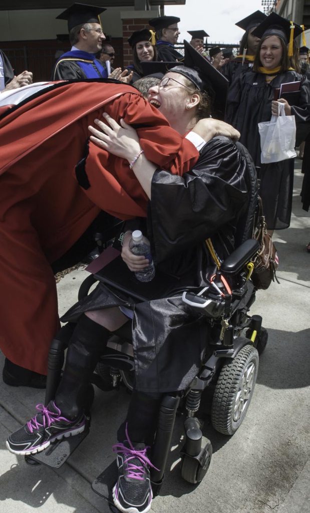 student in wheelchair is hugging a faculty member