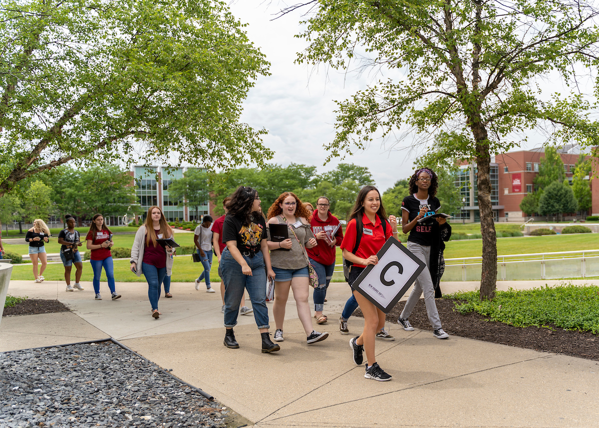 A New Hounds Day orientation leader is walking on campus with a group of new students.