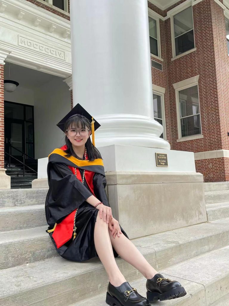 Rongjie Wang poses on the steps of Good Hall in commencement regalia