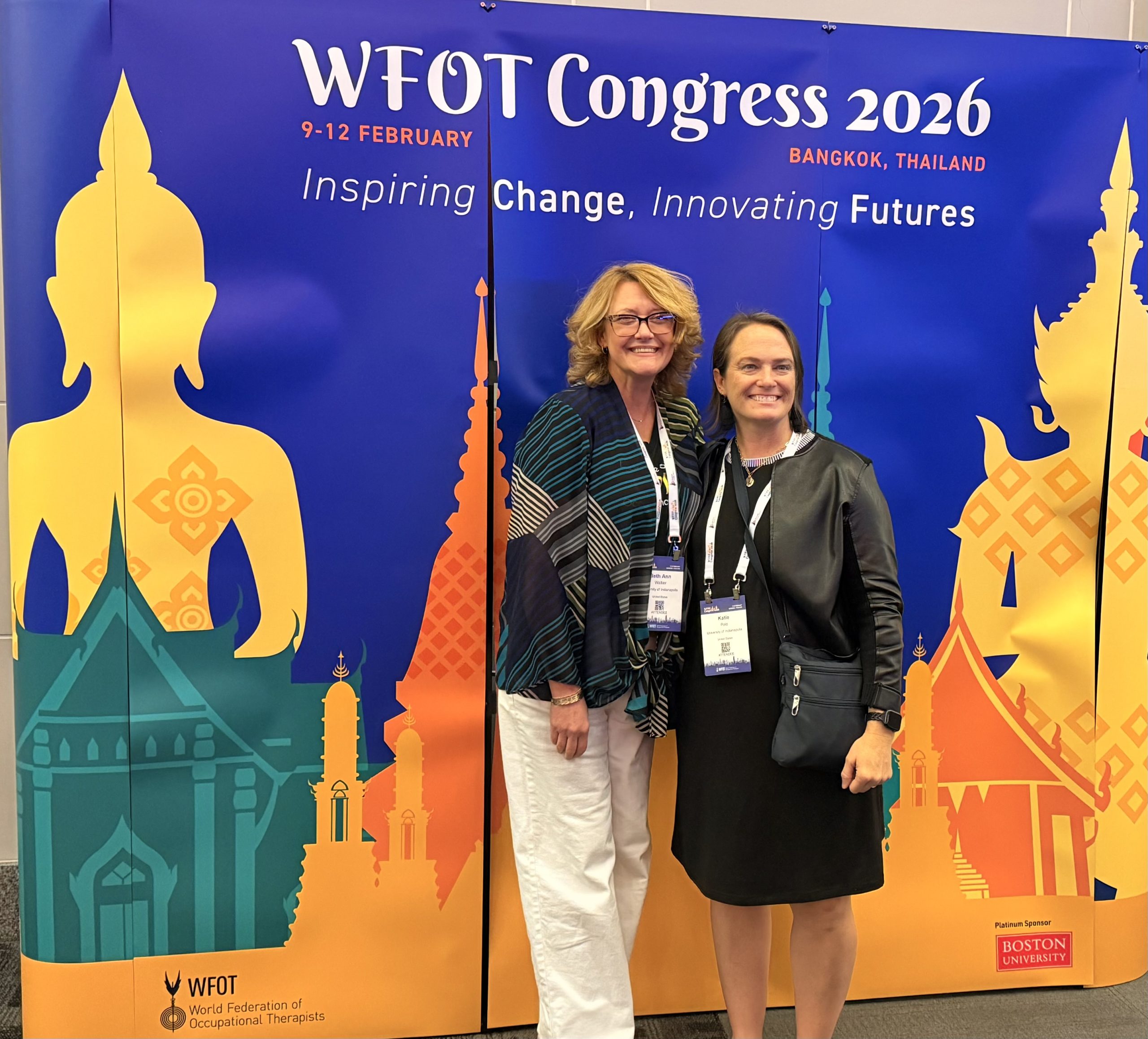 Dr. Beth Ann Walker and Dr. Katie Polo in front of banner for the WFOT Congress 2026
