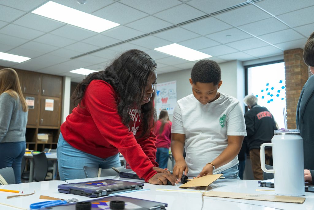 UIndy student helps elementary student build something on table in classroom 