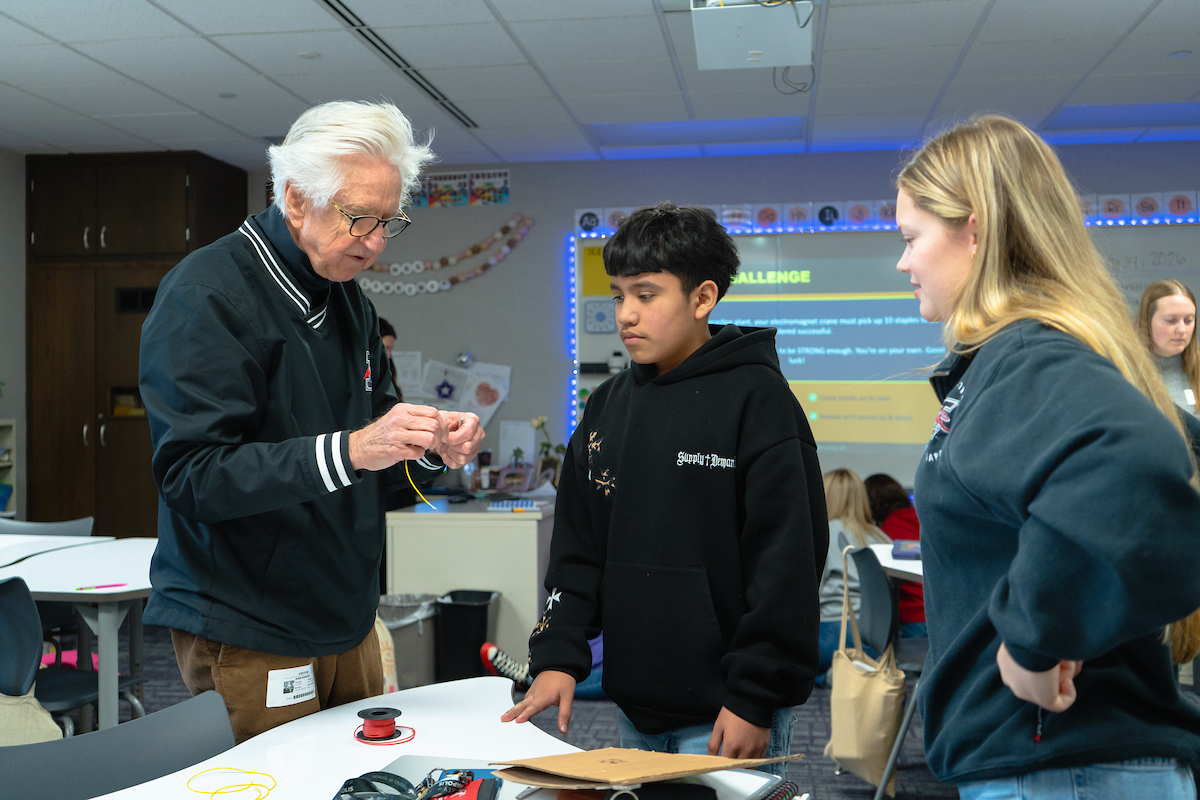Man shows boy how to build something with a college student watching inside a classroom