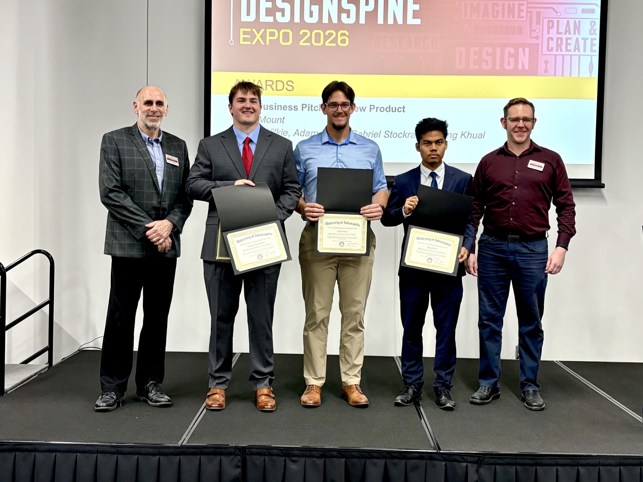 Three students holding up certificate on stage with DesignSpine backdrop with teachers at their sides