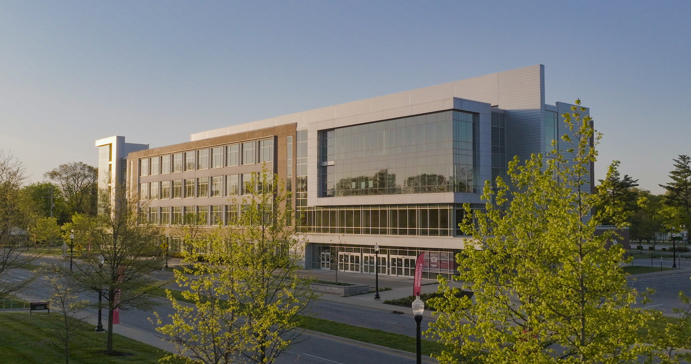 Wide view of UIndy building in the shining sun with trees in the foreground