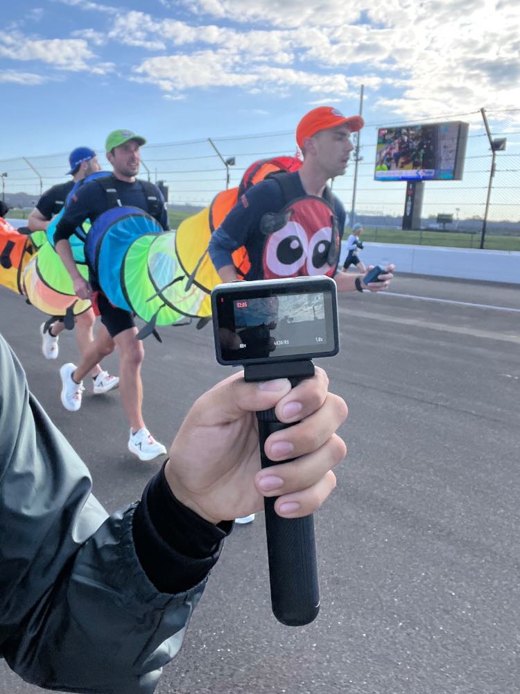 Stopwatch in front of five runners in caterpillar costume with race track in background