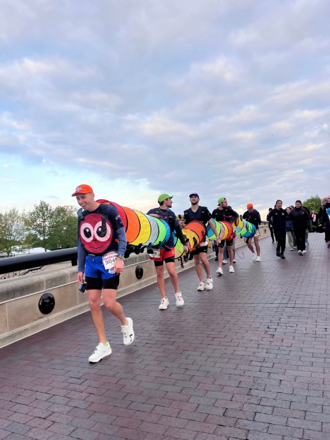 Five men in caterpillar costume walk on bridge. Man in front of laughing