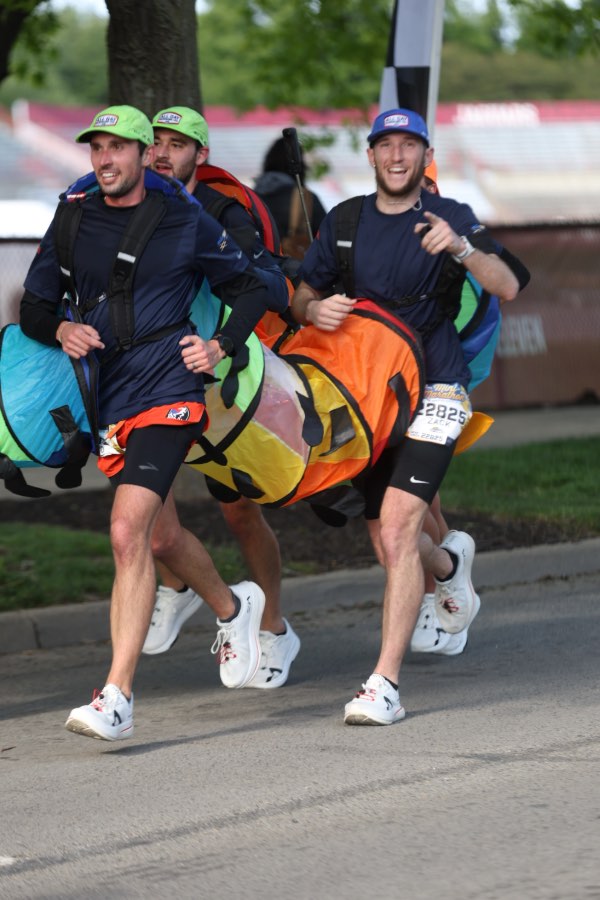 Men wearing hats and five-person rainbow-colored caterpillar costume run in marathon