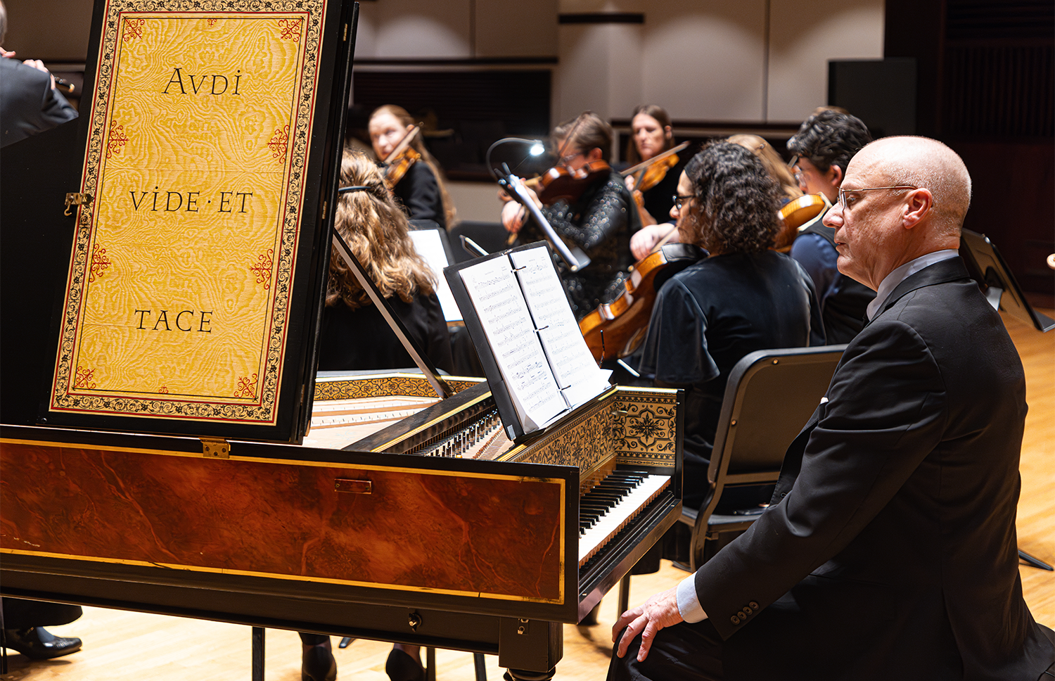 Photo of Tom Gerber, harpsichordist, with the Indianapolis Baroque Orchestra. Text decorating the harpsichord reads "Audi, vide, et tace."