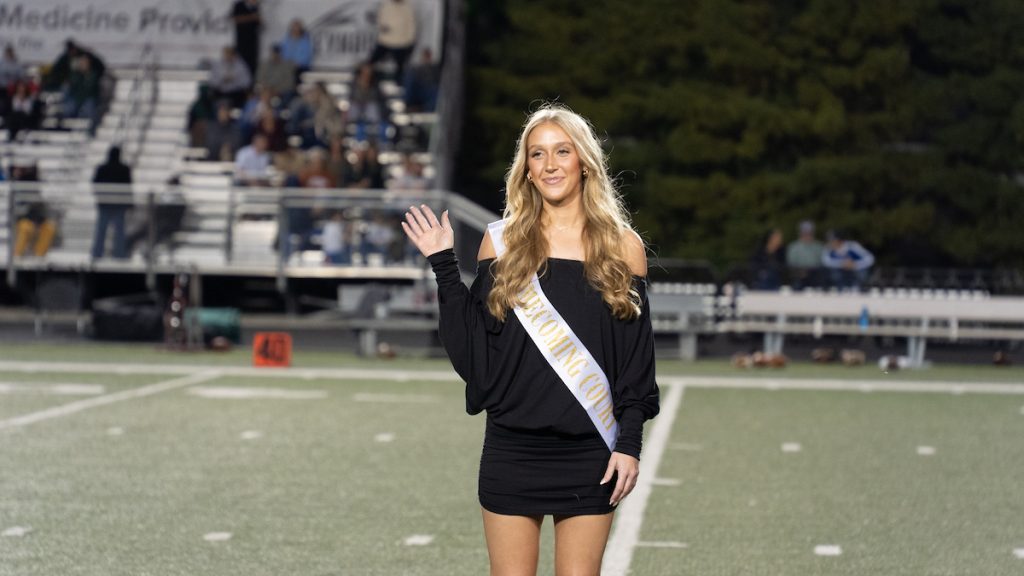 Maddie Pennington, dressed in a black outfit and wearing a sash that reads, "Homecoming Court."